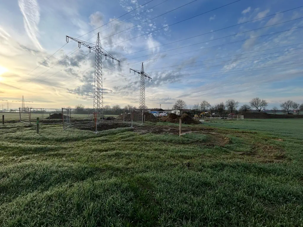 Eine Kabeltrasse ist bei Dämmerung zu seheen. Im Hintergrund ist ein Umspannwerk sichtbar.