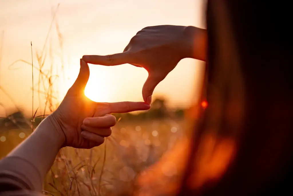 Eine Hand, die eine Raute formt um ein Ziel zu markieren. Im Hintergrund ist ein Sonnenuntergang sichtbar.